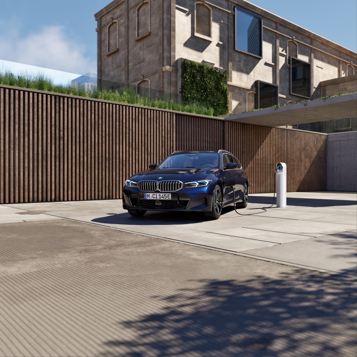 Person charging a blue electric car at an outdoor charging station next to a modern house with glass walls.